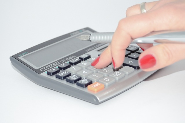 Mão com as unhas pintadas de vermelho usando uma calculadora e segurando uma caneta