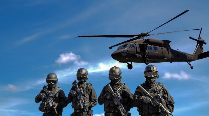 Foto de quatro militares com um helicóptero voando ao fundo